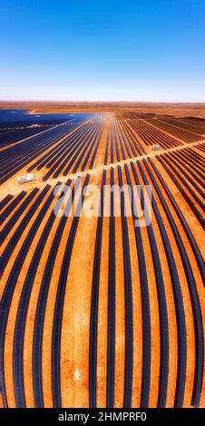 Linien von Solarpaneelelementen der Broken Hill Solaranlage auf rotem Boden im australischen Outback - vertikales Luftpanorama. Stockfoto