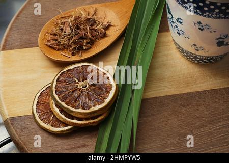 Goiânia, Goias, Brasilien – 11. Februar 2022: Zitronengrasblätter, ein paar Scheiben dehydrierte Orange, ein Löffel Kräuter, auf einer Holzoberfläche. Stockfoto