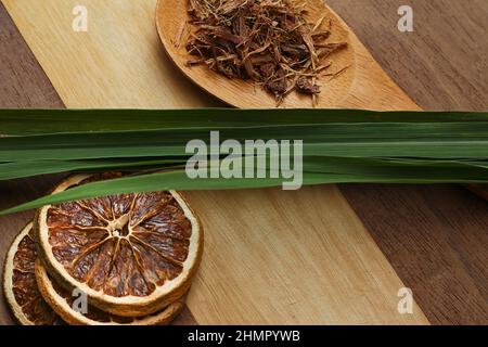 Goiânia, Goias, Brasilien – 11. Februar 2022: Zitronengrasblätter, ein paar Scheiben dehydrierte Orange, ein Löffel Kräuter, auf einer Holzoberfläche. Stockfoto