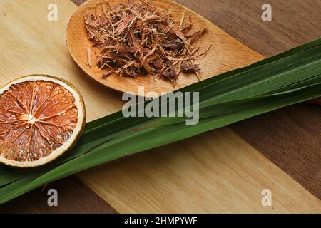Goiânia, Goias, Brasilien – 11. Februar 2022: Zitronengrasblätter, ein paar Scheiben dehydrierte Orange, ein Löffel Kräuter, auf einer Holzoberfläche. Stockfoto