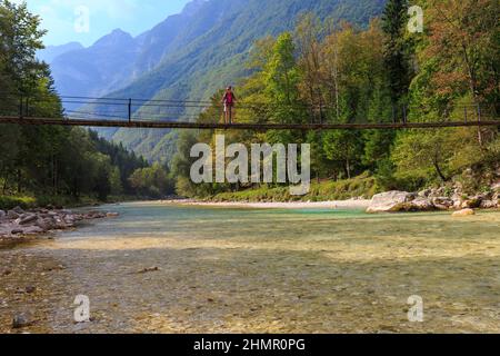 Eine Frau überquert die Swing Bridge über dem kristallklaren Wasser des Flusses Soča, Zugang zum Camp Soča, Slowenien Stockfoto