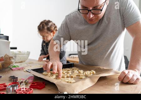 Beschnittene Ansicht eines nicht erkennbaren Mannes und seiner Tochter, die mit Keksschneidern auf der Schneide Süßigkeiten machten. Vater Plätzchen auf das Backblech legen Stockfoto