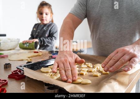 Beschnittene Ansicht eines nicht erkennbaren Mannes und seiner Tochter, die mit Keksschneidern auf der Schneide Süßigkeiten machten. Vater Plätzchen auf das Backblech legen Stockfoto