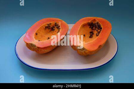 Papaya halbiert auf weißem Teller mit blauem Rand auf blauem Hintergrund Stockfoto