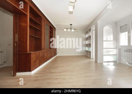 Wohnzimmer mit maßgefertigtem Holzbücherregal aus Mahagoniholz, hellen Holzböden und eingebautem Regal neben der geschlossenen Terrasse Stockfoto
