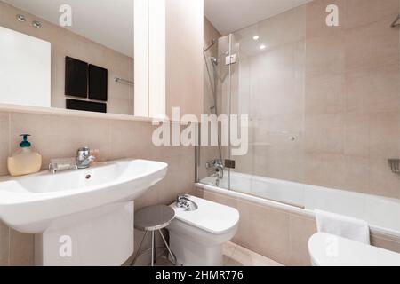 Modernes Badezimmer mit dunkelbraunen gefliesten Wänden, Dusche, weißen Toilettenschüsseln und cremefarbener Marmorplatte in einer Ferienwohnung Stockfoto