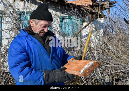 Zaitsewe, Donezk, Ukraine. 5th. Februar 2022. Ein alter Mann schaut auf einen alten Ziegel in der Nähe des 120 Jahre zerstörten verlassenen Hauses in den Außenbezirken von Zaitseve.US-Präsident Joe Biden hat alle in der Ukraine verbliebenen amerikanischen Bürger aufgefordert, das Land sofort zu verlassen, unter Berufung auf die zunehmende Bedrohung durch russische Militäraktion. Er sagte, dass er keine Truppen entsenden würde, um die Amerikaner zu retten, wenn Moskau die Ukraine einmarschiert. Der Kreml sagt, er wolle "rote Linien" durchsetzen, um sicherzustellen, dass sein ehemaliger sowjetischer Nachbar nicht der NATO Beitritt (Foto: © Andriy Andriyenko/SOPA Images via ZUMA Press Wire) Stockfoto