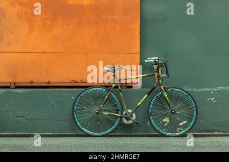 Ein Fahrrad vor einer orangefarbenen Stahltür mit einer grünen Lagerhauswand. Kopierbereich, selektiver Fokus. Stockfoto