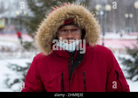 Porträt eines Mannes in einer roten Winter-Daunenjacke mit einer Brille und einem medizinischen Verband im Gesicht Stockfoto