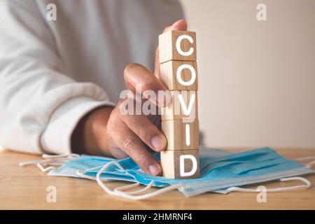 Dieses Konzept zeigt die Kampagne für das richtige Tragen der Maske. Holzblöcke mit Text, COVID. Blaue medizinische Maske auf dem Tisch. Krankheitsschutz wie Influenza, f Stockfoto