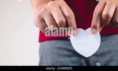Der Mann zeigt ein Papierherz an der Unterseite des Körpers. Nahaufnahme mit Kopierbereich. Stockfoto