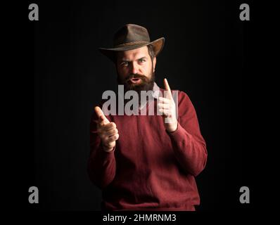 Bärtiger Cowboymann mit Cowboyhut. Wilde Westwaffen, Fingerrevolver schießen. Cowboy Mann zeigen Finger Pistole. Stockfoto