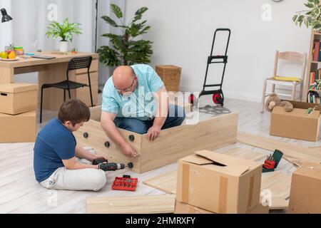 Papa steckt eine Möbelschraube in ein faltbares Bücherregal. Stockfoto