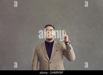 Porträt eines glücklichen Geschäftsmannes im Anzug und einer Brille, die den Finger nach oben zeigt, beeindruckt von einer großartigen Idee Stockfoto