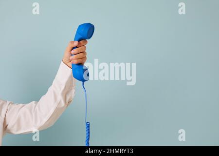 Menschliche Hand mit blauem Festnetzempfänger auf hellblauem Kopierraum-Hintergrund Stockfoto