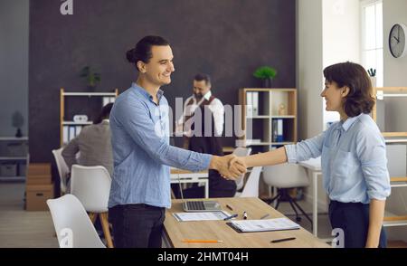 Junger Mann und reife Frau Händedruck im Büro nach Arbeitsbeschaffungsgespräch Stockfoto