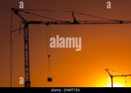 Sonnenuntergang hinter einer Silhouette mit Kränen auf einer Baustelle Stockfoto
