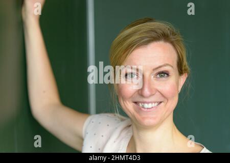 Nahaufnahme Porträt einer Lehrerin in der Klasse Schreiben auf der Tafel heute Lektion und Blick auf die Kamera mit freundlichem Gesicht Stockfoto