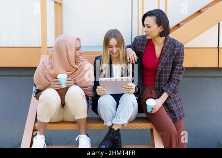 Stylische Freundinnen, die auf dem Tablet unterwegs sind und Kaffee zum Mitnehmen trinken Stockfoto
