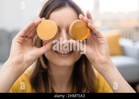 Eine junge Frau hält Kosmetikcreme in Metallbehältern in den Händen und versteckt ihre Augen Stockfoto