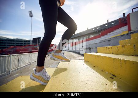 Zugeschnittenes Bild von weiblichen Beinen, die die Betontreppe hochlaufen. Seitenansicht Stockfoto