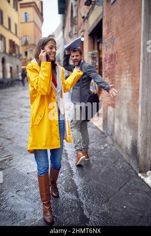 Eine junge Frau, die an einem regnerischen Tag auf der Straße geht und entspannt am Telefon telefoniert und sich nicht um Passanten kümmert, die sie getroffen hat. Gehen, Regen, Stockfoto