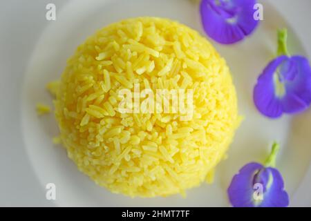 Kurkuma-Reis- und Schmetterlingsblüten auf weißem Teller. Nahaufnahme. Tabellenansicht von oben. Stockfoto