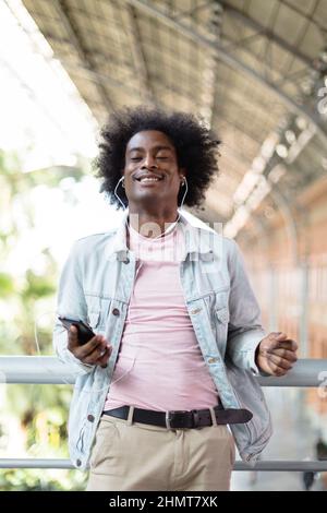 Glücklicher afroamerikanischer Mann, der Musik von seinem Telefon genießt. Positive Emotionen, Lifestyle und Glück. Stockfoto