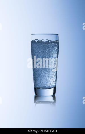 Wasserglas mit Kohlensäure auf blauem Hintergrund mit reflektierendem Trinkwasser Stockfoto