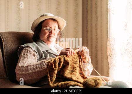 Ältere Frau strickt Pullover für ihre Enkel am Fenster Stockfoto