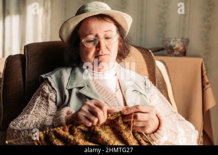 Ältere Frau strickt Pullover für ihre Enkel am Fenster Stockfoto