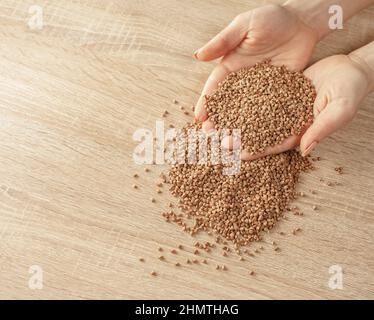 Roher Buchweizen in den Händen auf Holzhintergrund Stockfoto
