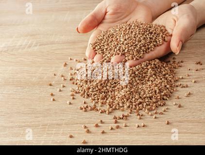 Roher Buchweizen in den Händen auf Holzhintergrund Stockfoto