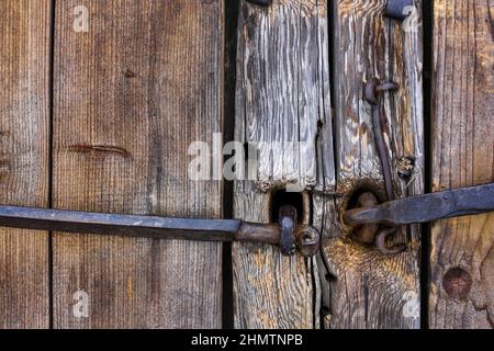 Altes Blockhaus. Türen, Tore. Geschmiedete Türgriffe aus rostetem Metall, Schrauben, Scharniere, Haken. Schäbiger Baum, gealterte Holzstruktur. Stockfoto