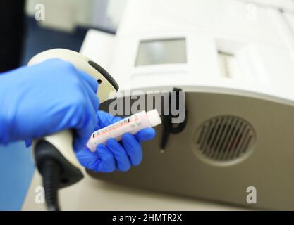 In einem modernen biochemischen Labor scannt ein Medizintechniker mit blauen Gummihandschuhen den Code des Reagenzrohrs. Stockfoto