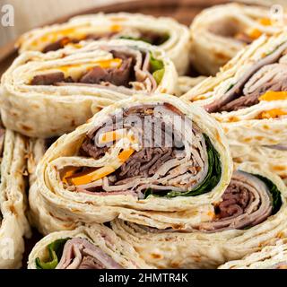 Nahaufnahme von Tortilla-Wraps, die mit Roastbeef, truthahn und Käse in einem Stapel auf einem Teller geschnitten wurden Stockfoto