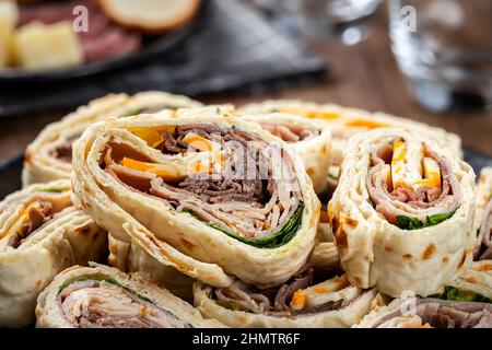 Nahaufnahme von Tortilla-Wraps, die mit Roastbeef, truthahn und Käse in einem Stapel auf einem Teller geschnitten wurden Stockfoto