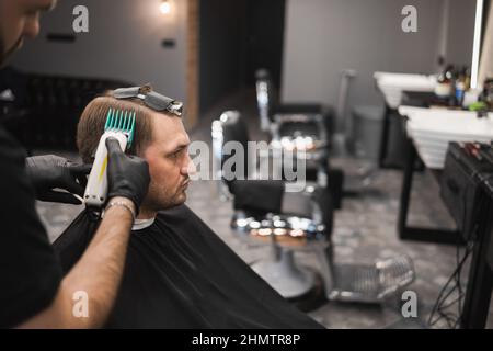 Barber Master macht einen modischen Haarschnitt für einen männlichen Kunden. Friseur schneidet einem Mann die Haare Stockfoto