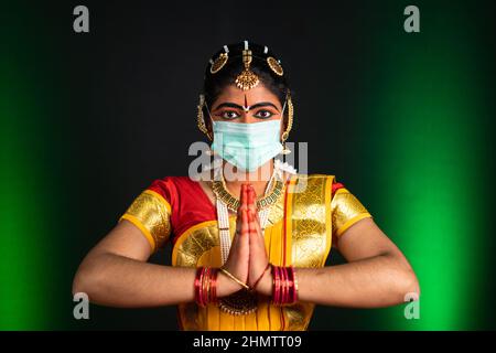 Portraitaufnahme der Bharatnatyam-Tänzerin mit medizinischer Gesichtsmaske, die beim Betrachtend der Kamera Namaste macht - Schutz vor Covid-19 Stockfoto