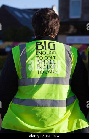 Slogan auf der Rückseite der Weste - groß genug, um fertig zu werden, klein genug, um sich zu kümmern. Stockfoto