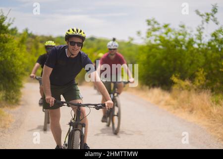 Der blonde und fitte Kerl fährt auf seinem Fahrrad und lächelt seinen Frineds hinter ihm zu Stockfoto