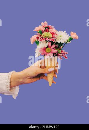 Weibliche Hand hält Eiscreme Waffel Kornett mit pastellrosa Rosen und andere verschiedene Blumen über sehr peri Hintergrund. Valentinstag oder Frauentag Stockfoto