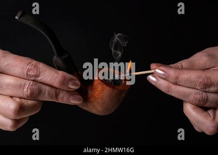 Weibliche Hände zünden eine Holzpfeife mit einem beleuchteten Streichholz an Stockfoto