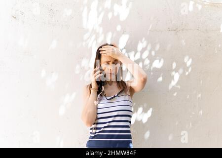 Gestresste junge Erwachsene Frau mit der Hand auf der Stirn, die schlechte Nachrichten im Smartphone-Gespräch erhält. Stockfoto