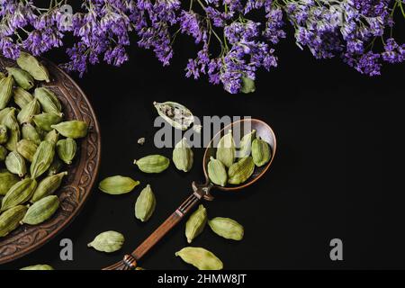 Trockene grüne Kardamom-Samen, Elettaria cardamomum, auf schwarzem Hintergrund in Vintage cooper orientalischen Design Schale und Löffel.Kardamom-Hülsen auf schwarzem Hintergrund Stockfoto