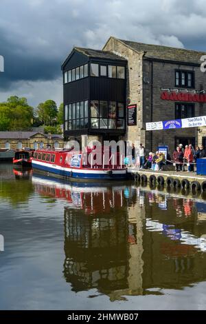 Männer, Frauen, die sich auf einem roten schmalen Boot (Ticketschalter, Anlegestellen am Kanal) für ein touristisches Freizeiterlebnis anstellen - Leeds-Liverpool Canal, Yorkshire, England, Großbritannien. Stockfoto