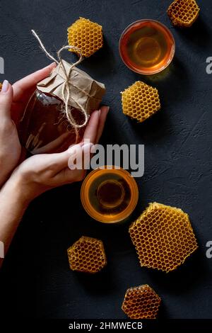 Hände einer Frau, die ein Glas mit Bienenhonig auf schwarzem Hintergrund hält. Speicherplatz kopieren. Stockfoto