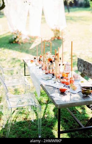 Tisch bedeckt mit einer weißen Tischdecke mit Kerzen, Früchten und Tassen im Garten Stockfoto