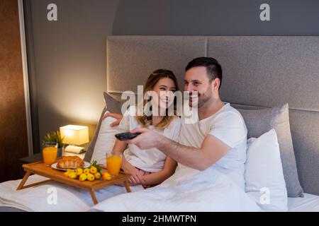 Portrait des glücklichen Paares, das im Schlafzimmer liegt und fernsieht.Paar, das sich vorbereitet, um einen Film zu sehen. Stockfoto