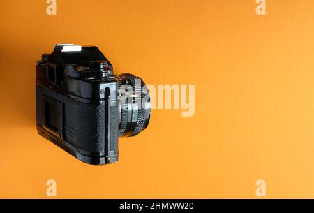 Klassische slr-Kamera aus der Ära der Filmfotografie - Seitenansicht auf orangefarbenem Hintergrund Stockfoto